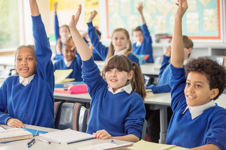 children in classroom raising hands